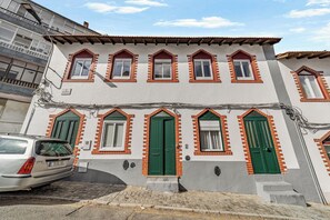 A two-story building with a row of windows and doors, a car parked in front, and a cobblestone street. - Setúbal Arena III, By Home Match (Setúbal)