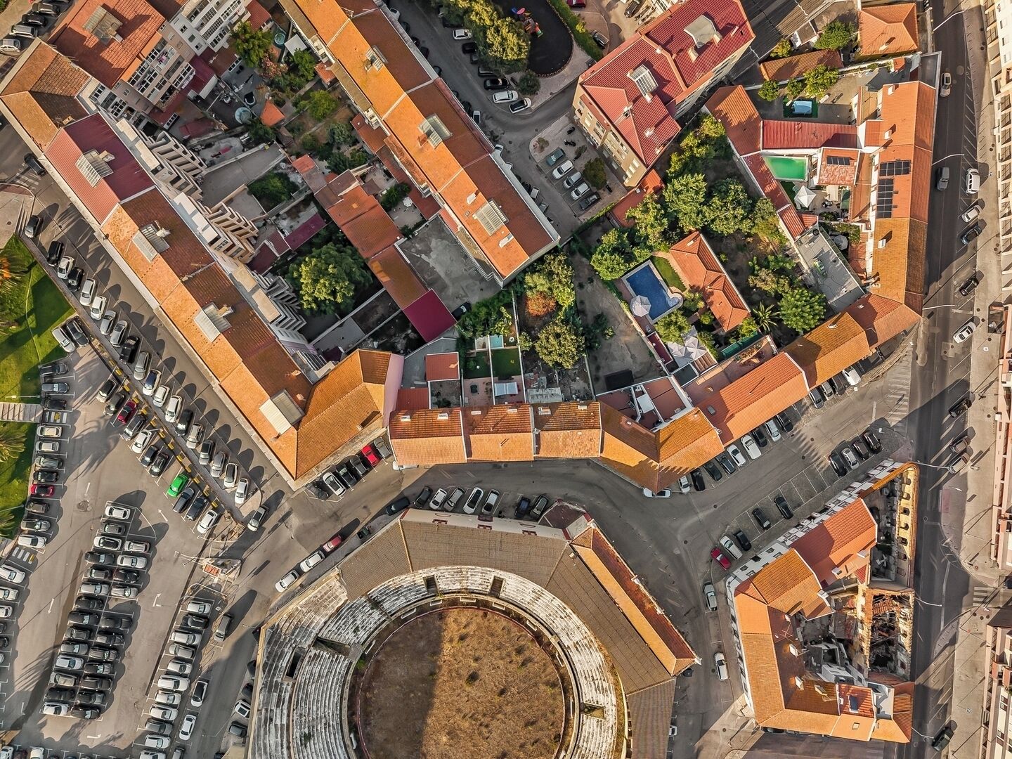 Vue aérienne d’un pâté de maisons comprenant une place circulaire, des immeubles aux toits recouverts de tuiles rouges et des voitures garées.