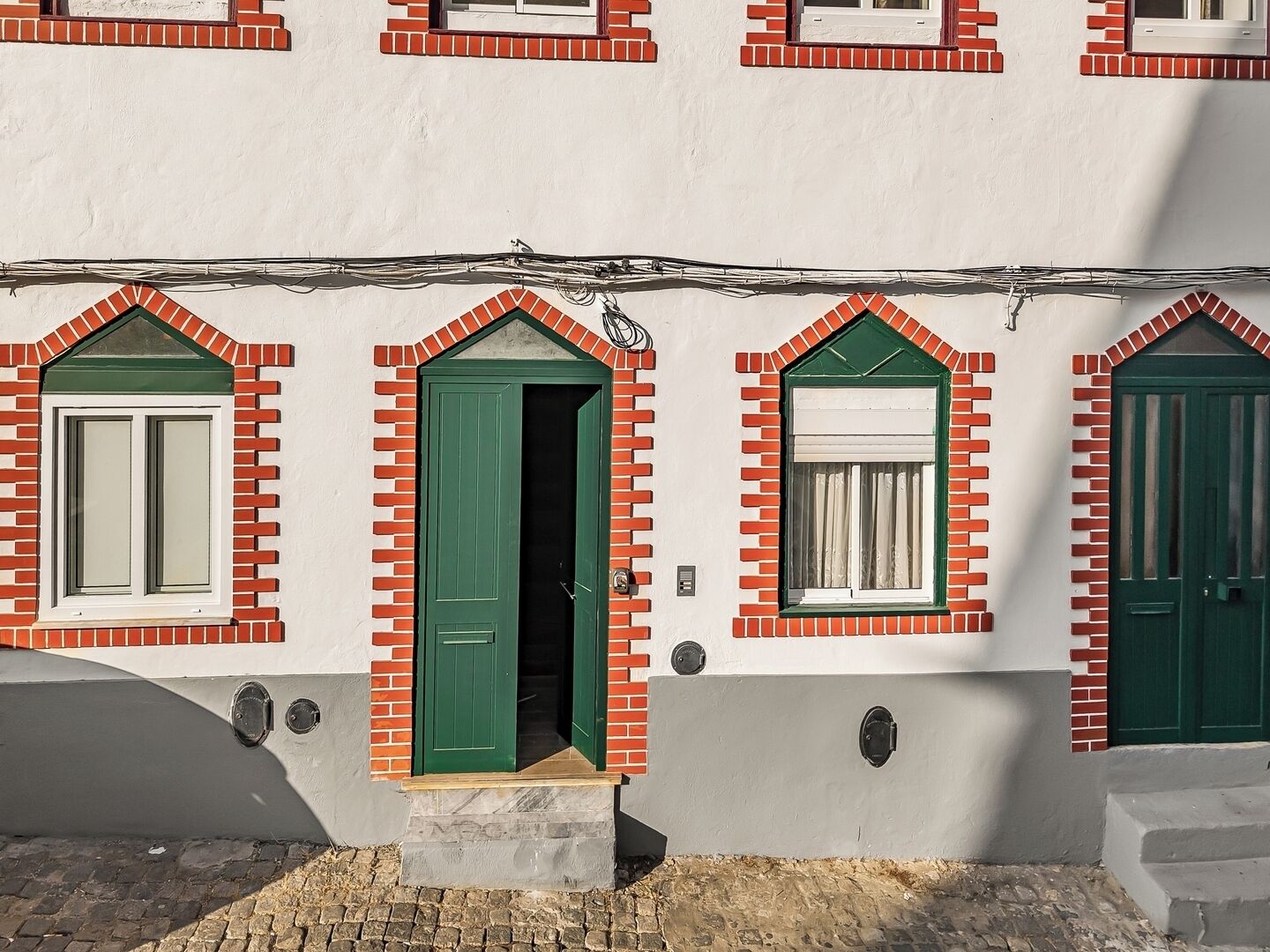 A building with a white facade, red brick window frames, and green doors.