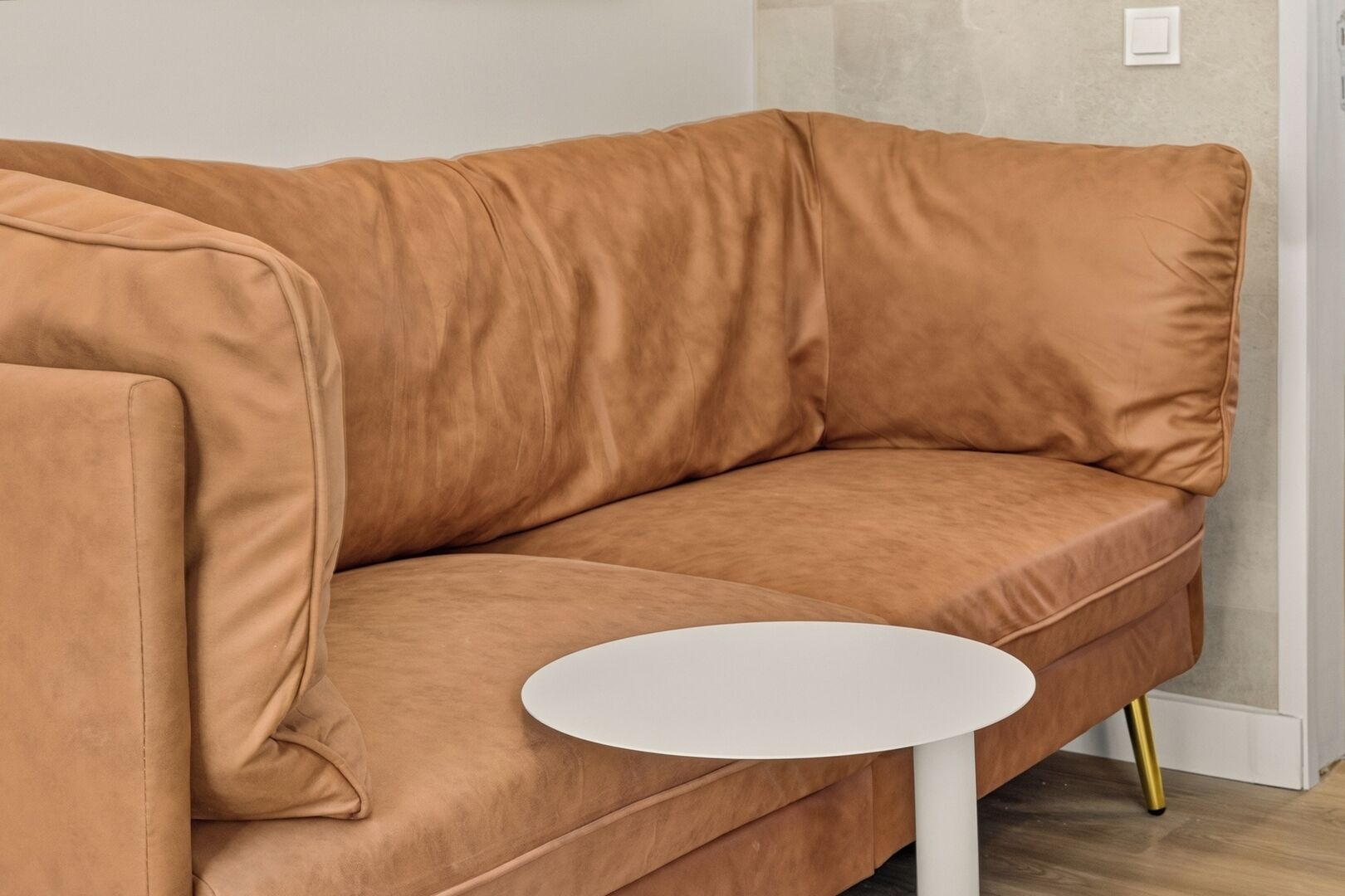 A tan-colored sofa with a round white table in front of it.