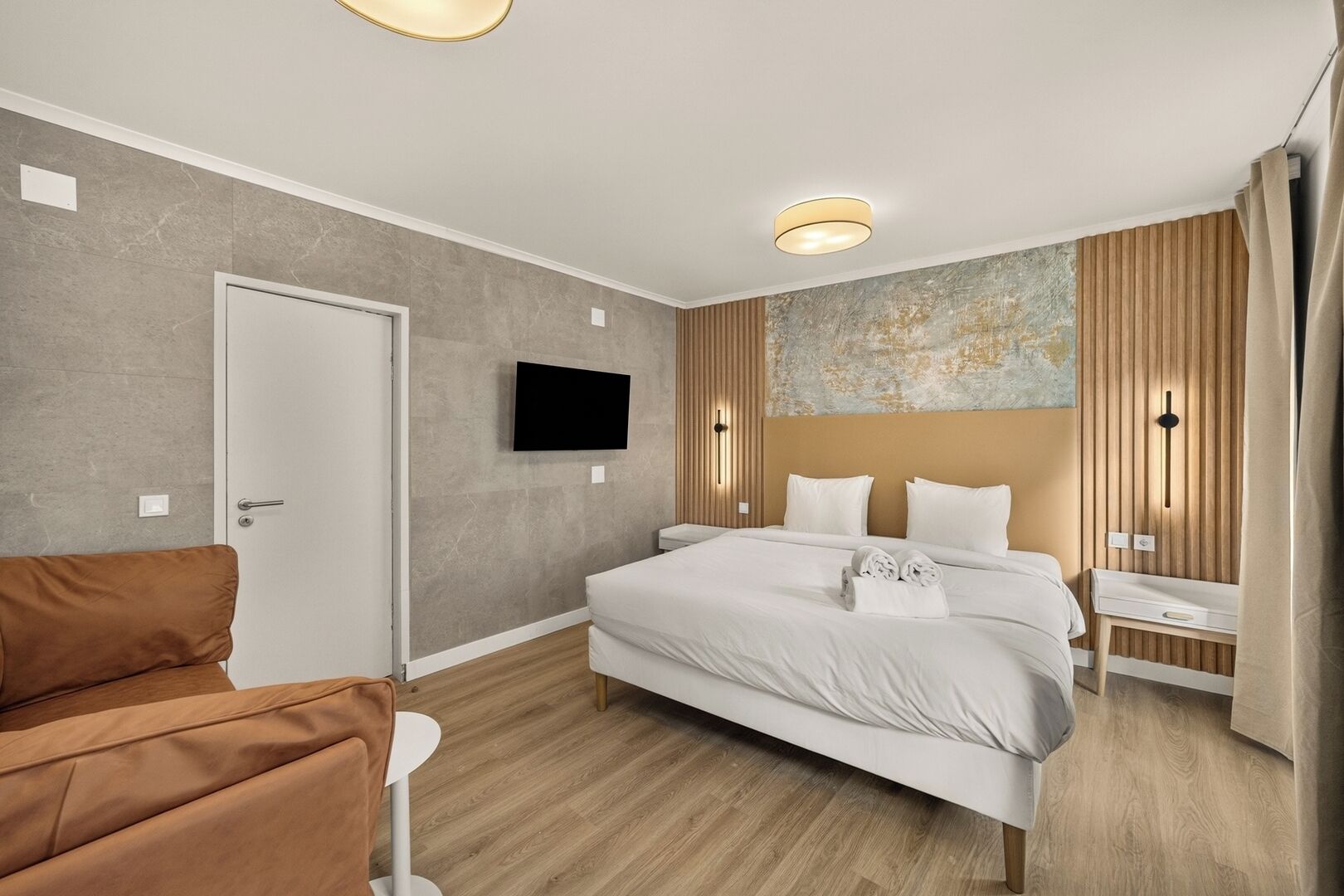A modern hotel room with a bed, a TV, a desk, and a chair.