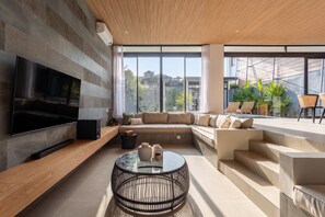 Ein modernes Wohnzimmer mit Flachbildfernseher, einem Ecksofa, einem Couchtisch und einer Treppe zu einem Balkon mit Sitzgelegenheit.