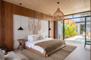 A modern bedroom with a large bed, wooden panel walls, macramé wall decor, and a view of a pool and greenery. - Brand New Opulent Villa, Huge Pool, Best Location (Badung Regency)