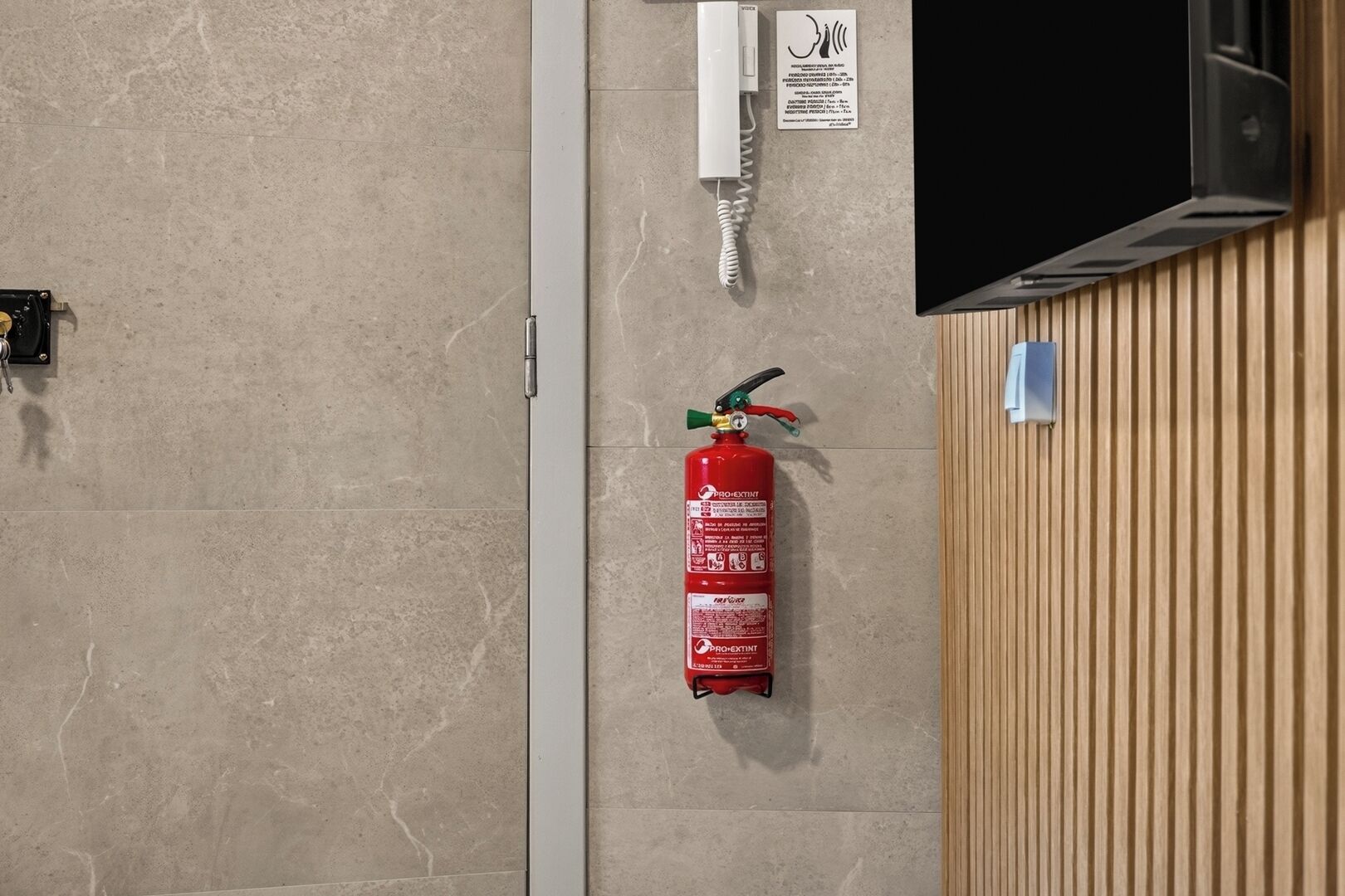 Ein an der Wand befestigter Feuerlöscher, ein Telefon und ein Fernseher.
