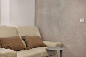 Ein modernes Wohnzimmer mit einem beigen Sofa, zwei braunen Kissen und einem kleinen runden Tisch.