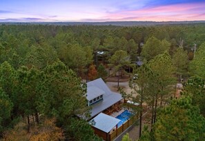 Ein Haus, umgeben von dichtem Wald, mit sichtbarem Schwimmbecken und einer Metallbedachung.