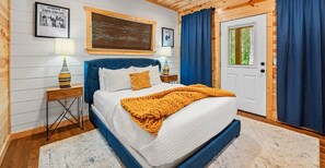 A bedroom with a bed, two bedside tables, a window, and a door. - NEW! Pool, Hot Tub, Pickleball, Rope Course, EV (Broken Bow)