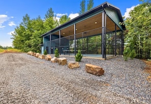A modern building with a covered outdoor area, surrounded by trees and a gravel path. - NEW! Pool, Hot Tub, Pickleball, Rope Course, EV (Broken Bow)
