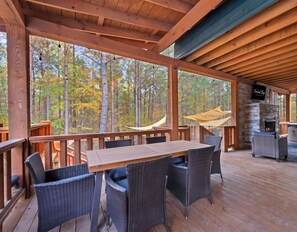 A wooden deck with a table and chairs, a hammock, and a stone fireplace. - NEW! Pool, Hot Tub, Pickleball, Rope Course, EV (Broken Bow)