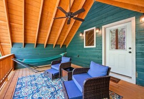 Eine überdachte Veranda mit Deckenventilator, einer Hängematte, Korbmöbeln mit Kissen und einem gemusterten Teppich.