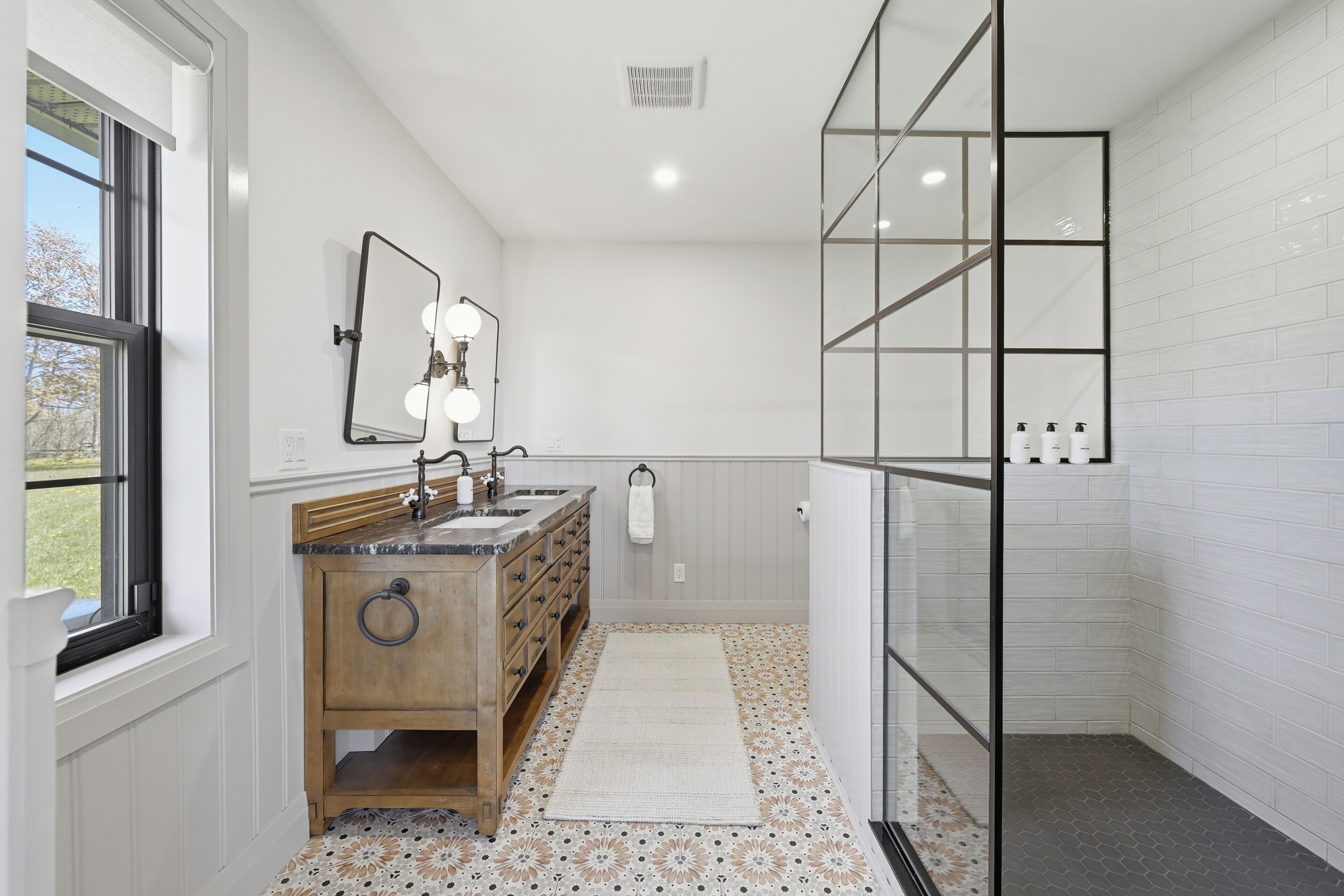 Une salle de bain avec un meuble-lavabo en bois, un miroir avec éclairage intégré, une douche avec des parois en verre et des carreaux de sol à motifs.