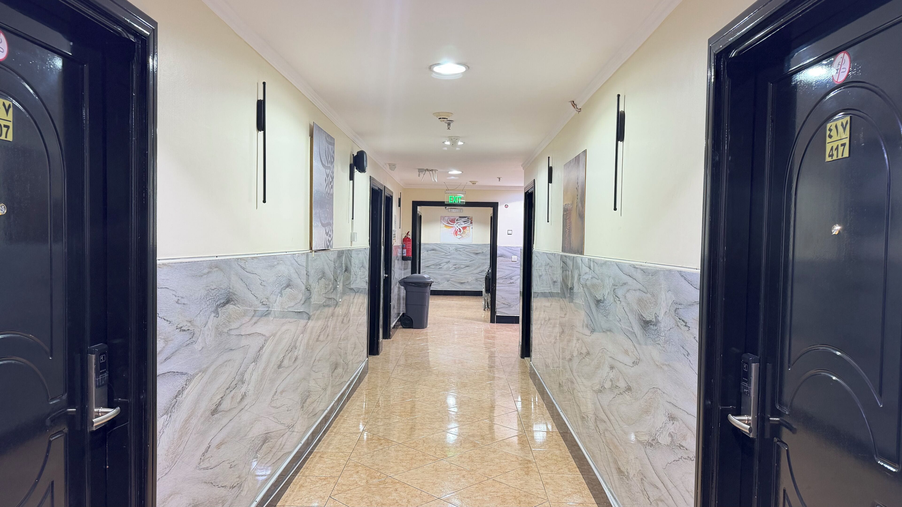 Un pasillo de hotel con suelo de mármol, puertas negras y un extintor en la pared.