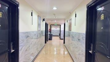 Un pasillo de hotel con suelo de mármol, puertas negras y un extintor en la pared.