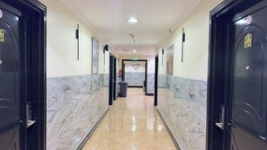 Un pasillo de hotel con suelo de mármol, puertas negras y un extintor en la pared.