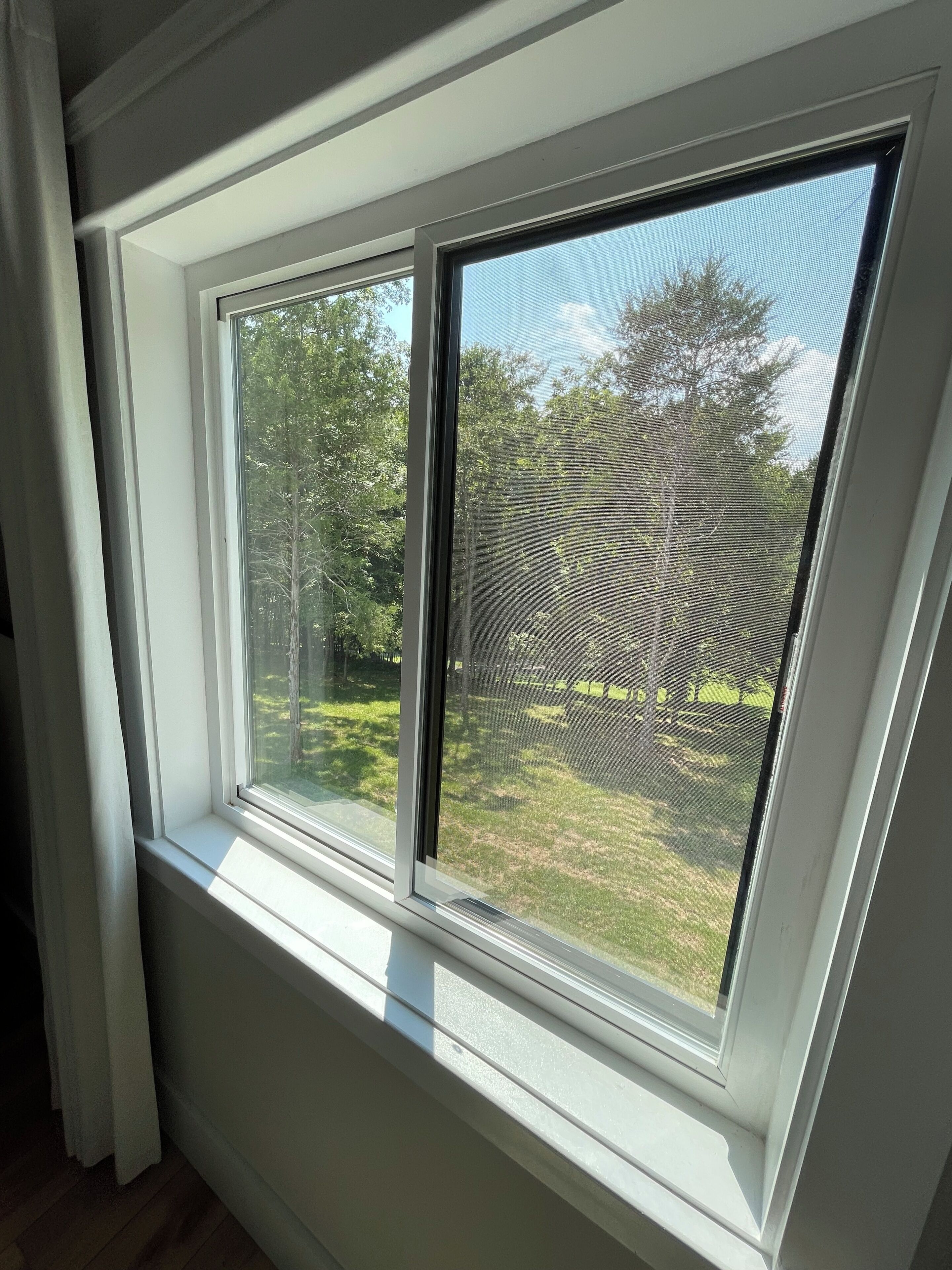 Une fenêtre donnant sur un espace verdoyant et des arbres.