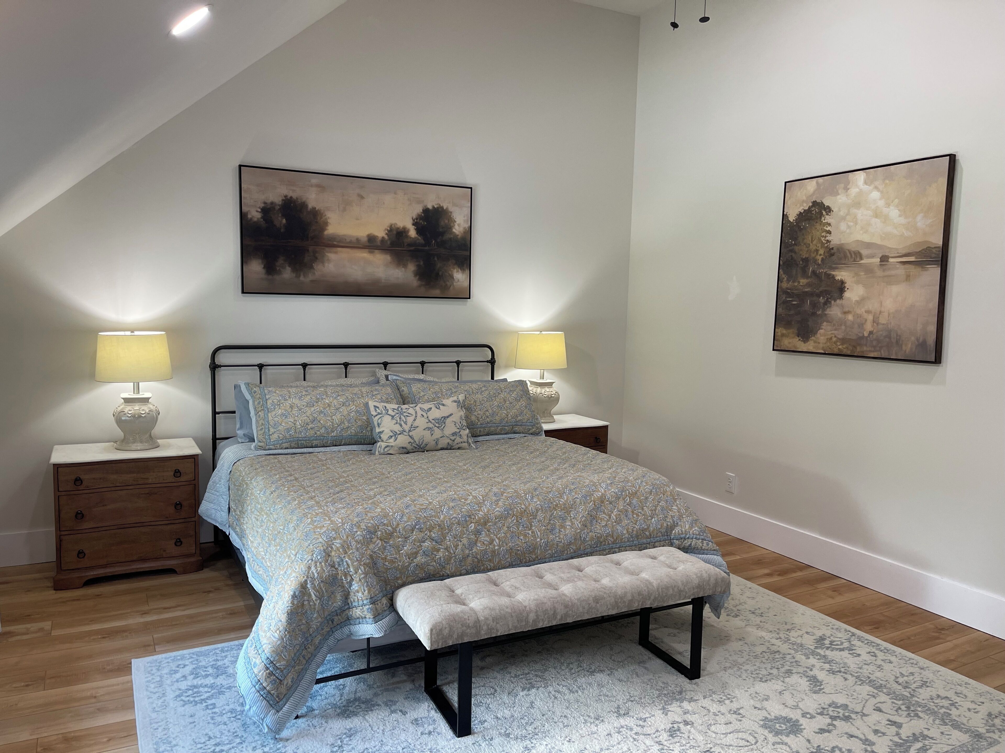 Une chambre à coucher comprenant un lit, deux tables de chevet, un banc et deux lampes fixées au mur.