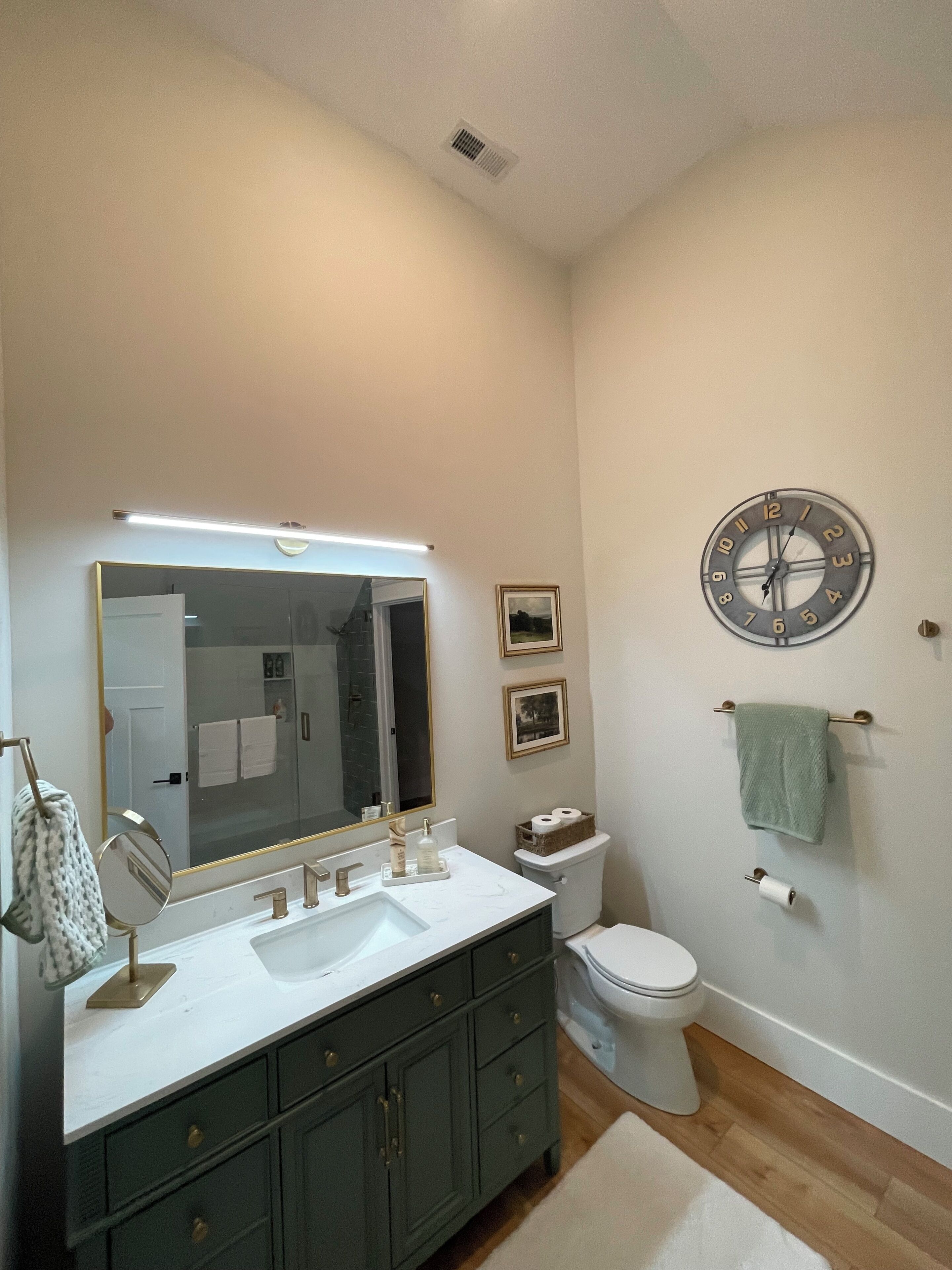 Une salle de bain avec un meuble-lavabo à deux vasques, des toilettes, un miroir et une horloge au mur.