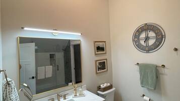 Une salle de bain avec un meuble-lavabo à deux vasques, des toilettes, un miroir et une horloge au mur.