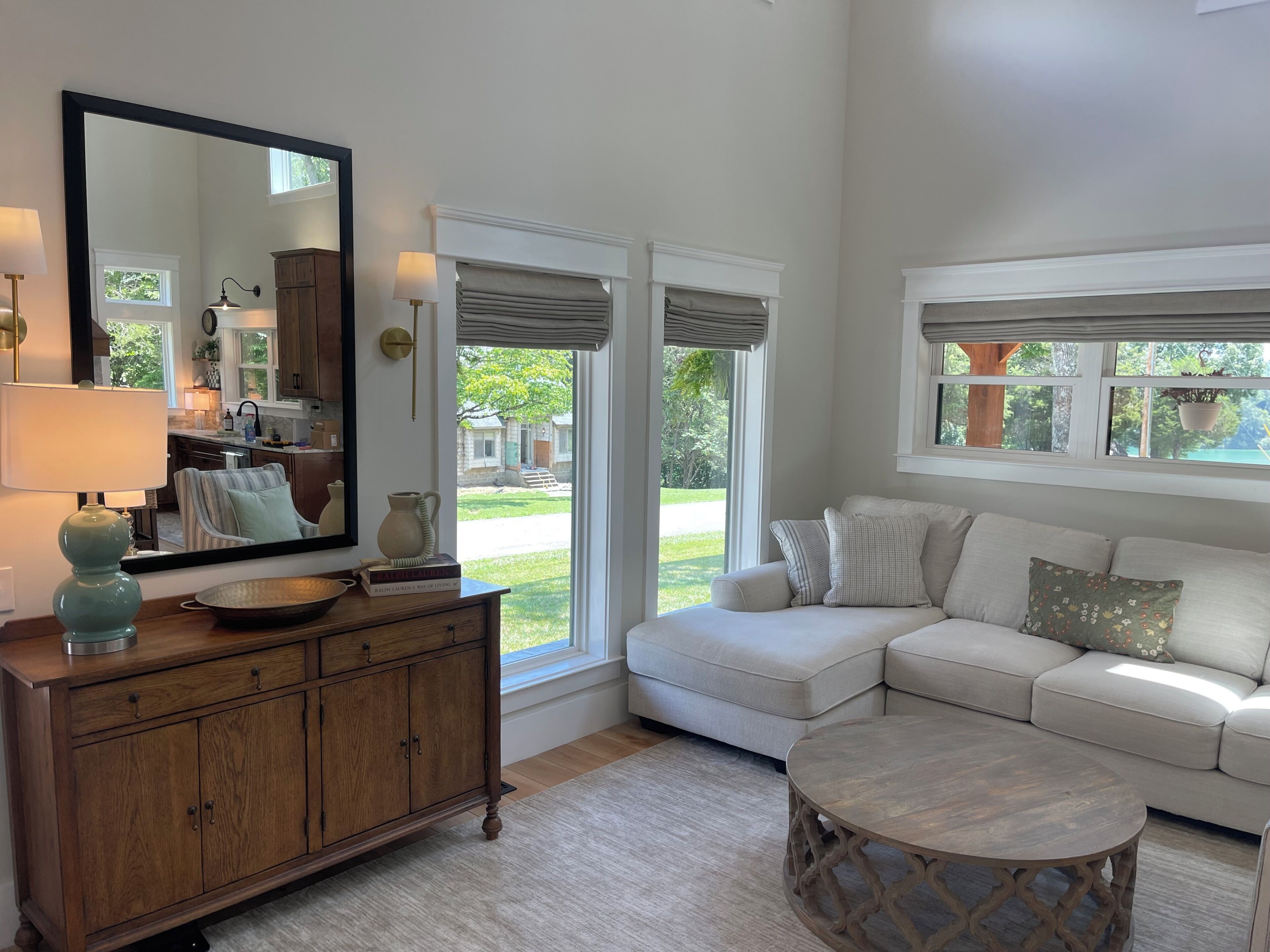 A living room with a sofa, a round coffee table, a wooden cabinet, a mirror, and a view of the outdoors.