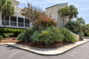 A residential area with a well-maintained garden, a white building with a balcony, and a palm tree. - Oyster Shell Villa by Sandpiper | Near Beach (Seabrook Island)