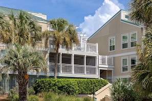A multi-story residential building with balconies, a covered outdoor area, and a well-maintained garden with palm trees. - Oyster Shell Villa by Sandpiper | Near Beach (Seabrook Island)