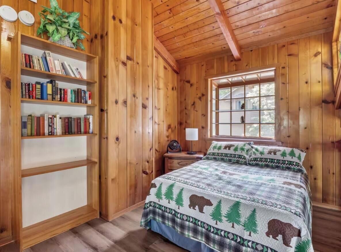 Quarto de cabana de madeira com uma cama, uma estante e uma janela.