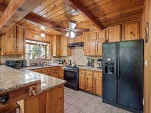 A kitchen with wooden cabinets, a black refrigerator, a stove, and a ceiling fan. - Near BassLake, sleeps 16, BBQ, Game Room (Bass Lake)