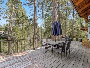 A wooden deck with outdoor furniture, a grill, and a view of a forest. - Near BassLake, sleeps 16, BBQ, Game Room (Bass Lake)