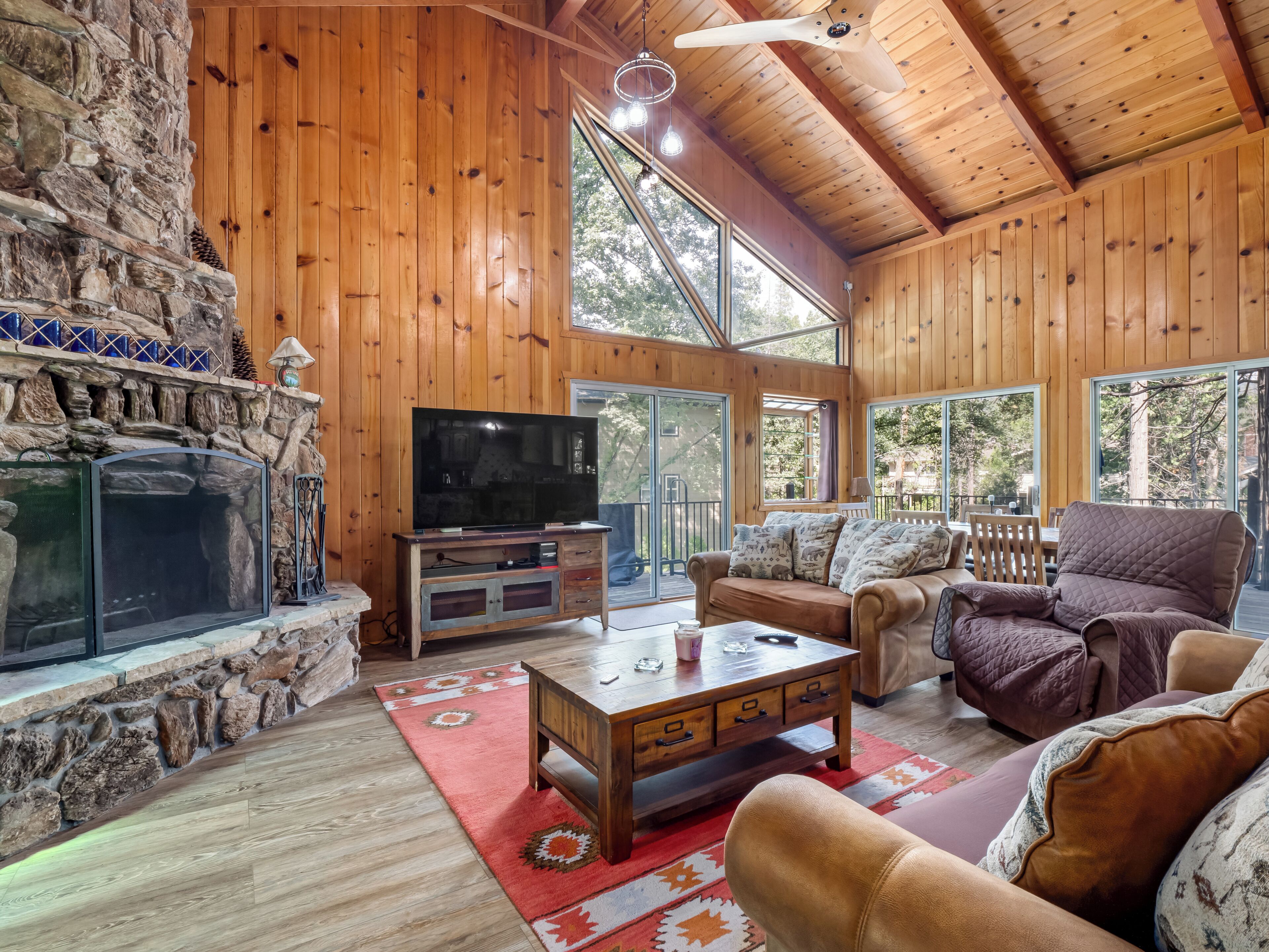 A cozy cabin interior with a stone fireplace, wooden walls, a television, and comfortable seating.