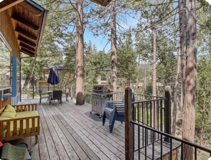 Une terrasse en bois, dotée de mobilier d’extérieur, d’un barbecue et offrant une vue sur une zone boisée.