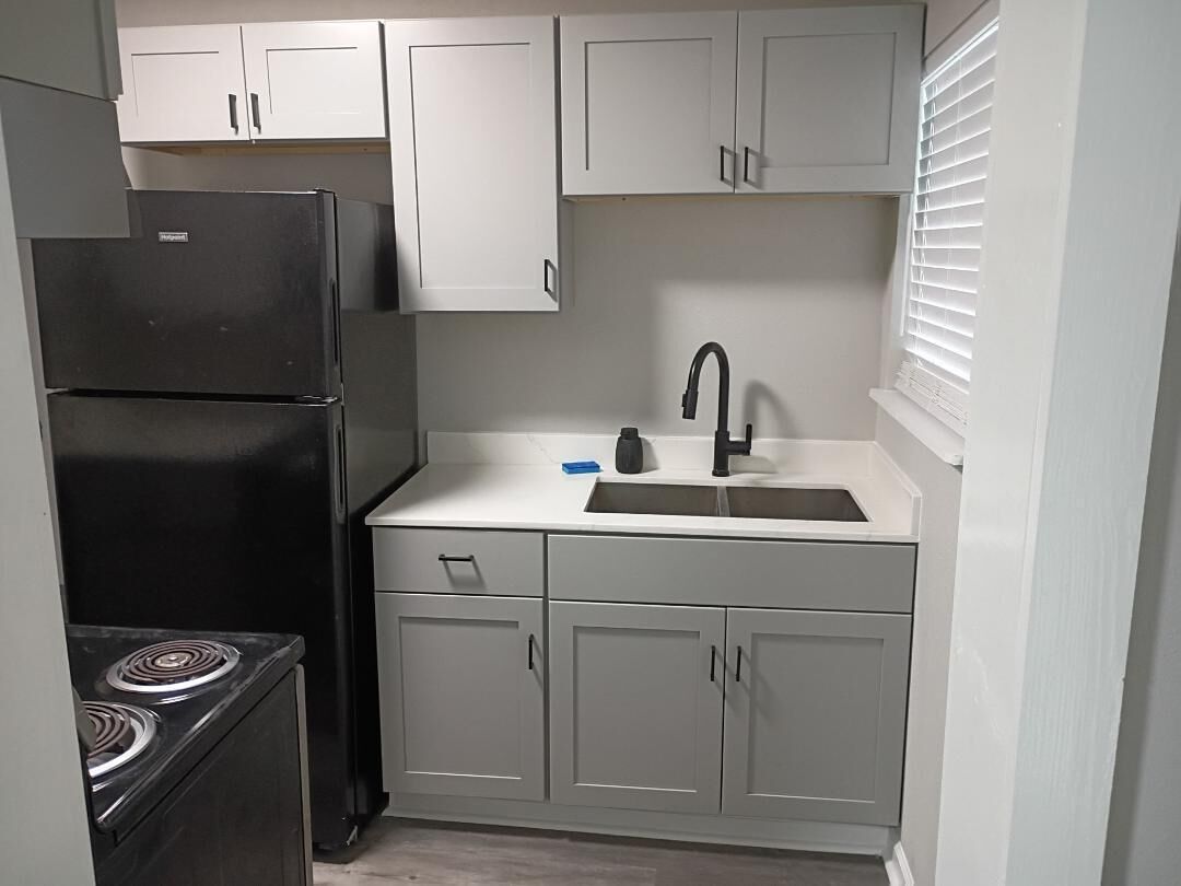 A compact kitchen with white cabinets, a black refrigerator, a stove, and a sink with a faucet.