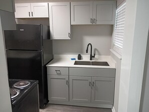 A compact kitchen with white cabinets, a black refrigerator, a stove, and a sink with a faucet.
