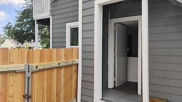 A residential building with a grey exterior, a wooden fence, and a door leading to an interior space.