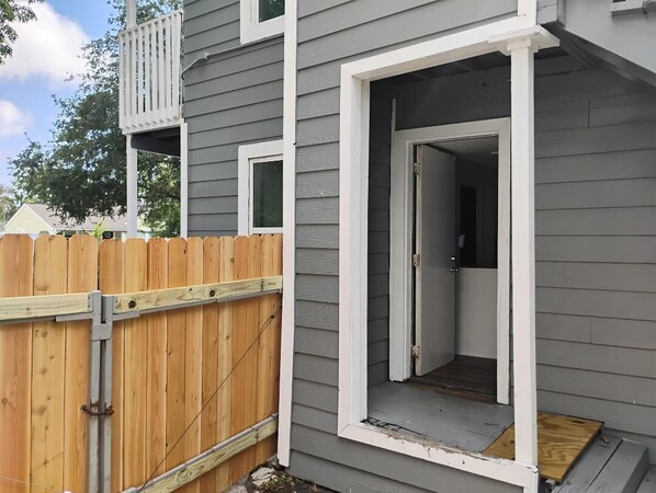 A residential building with a grey exterior, a wooden fence, and a door leading to an interior space.
