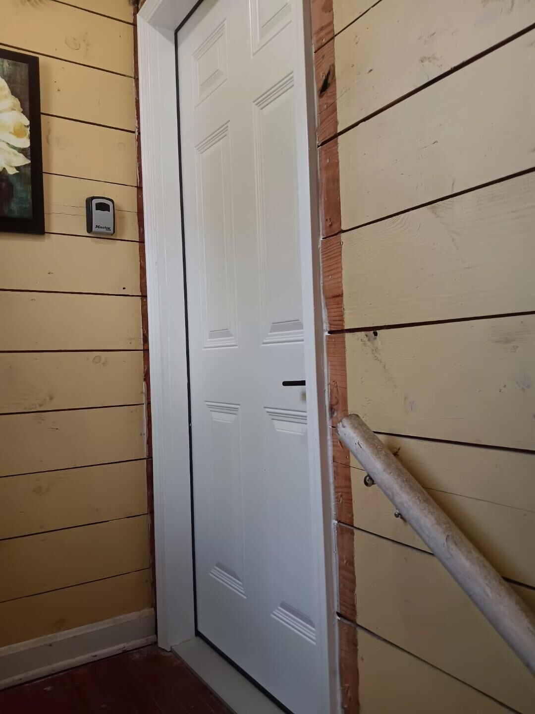 A white door with a metal handle, a small mailbox, and a wooden handrail.