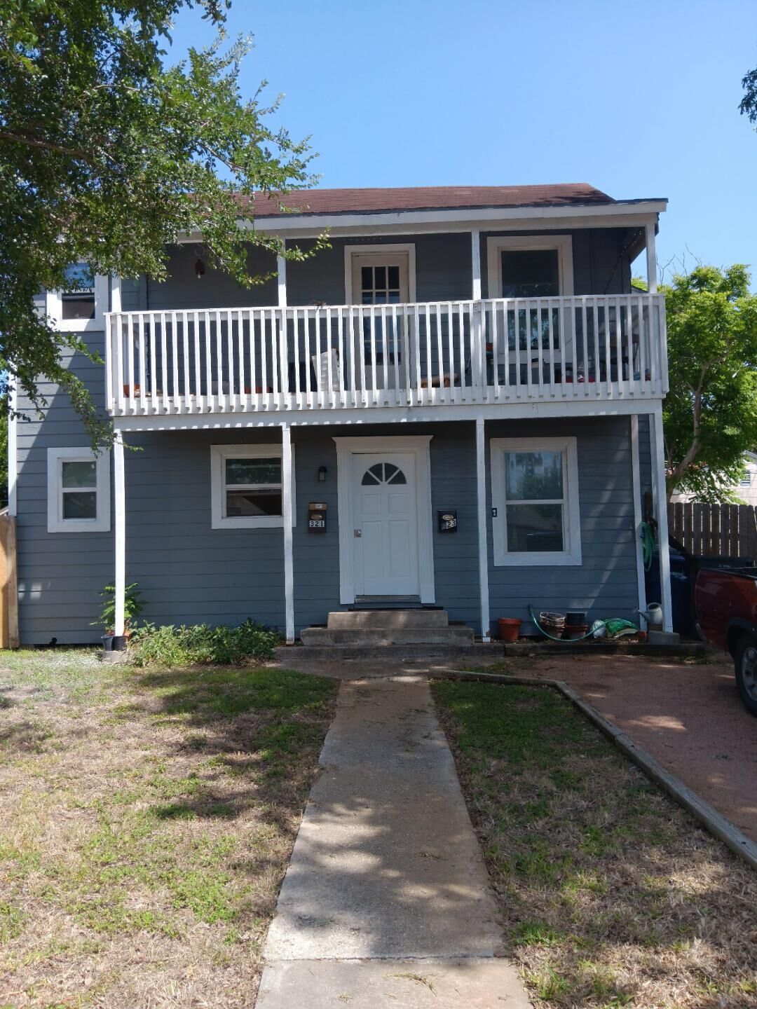 A two-story house with a front porch, a small front yard, and a driveway.