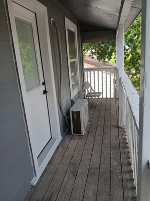 A covered porch with a white railing, a single chair, and a small heater.