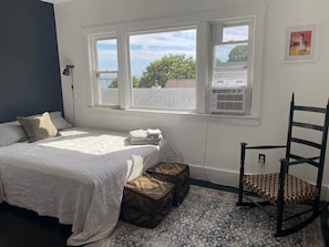 A bedroom with a bed, a chair, a window with a view, and a radiator. - Beachfront 2BR Penthouse Deck + Bay Views (Provincetown)