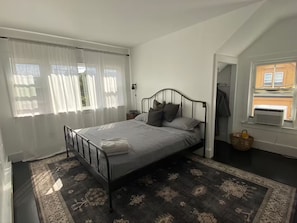 A bedroom with a single bed, a nightstand, a lamp, and a window with curtains. - Beachfront 2BR Penthouse Deck + Bay Views (Provincetown)