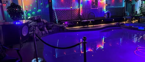 Espaço ao ar livre iluminado à noite, com piscina, iluminação decorativa e áreas de estar.
