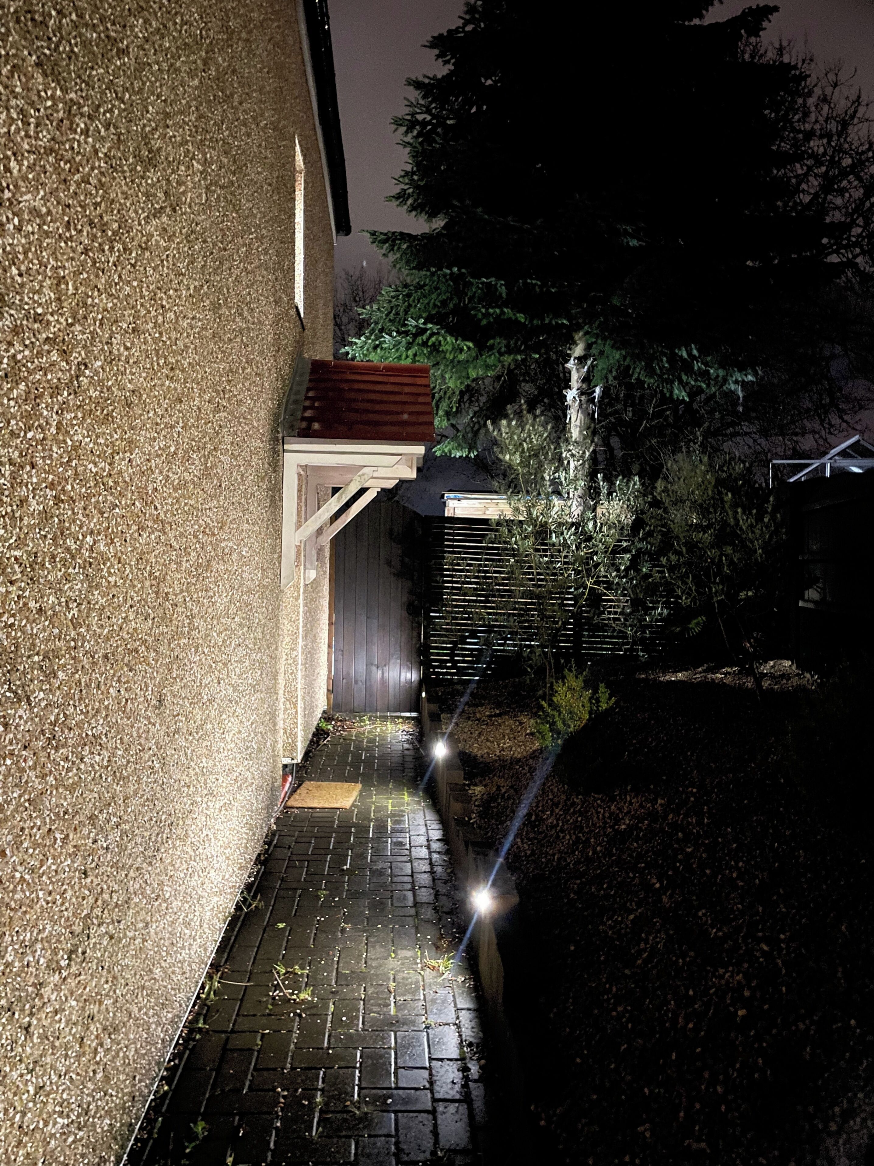 A pathway leading to a building with a textured wall and a wooden deck.