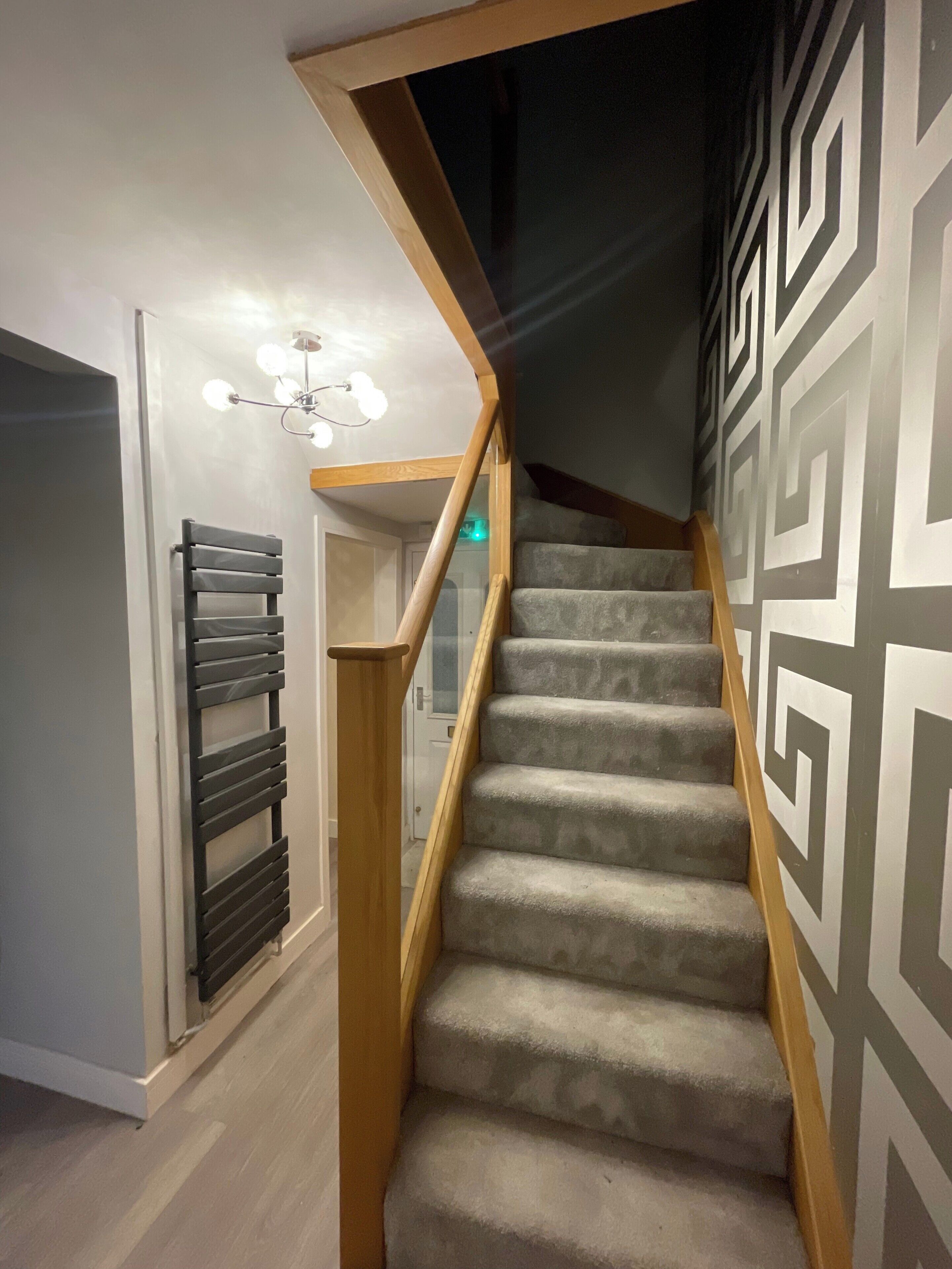 Una escalera con barandilla de madera y peldaños alfombrados que conduce a una habitación con lámpara en el techo.