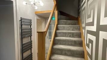 Una escalera con barandilla de madera y peldaños alfombrados que conduce a una habitación con lámpara en el techo.
