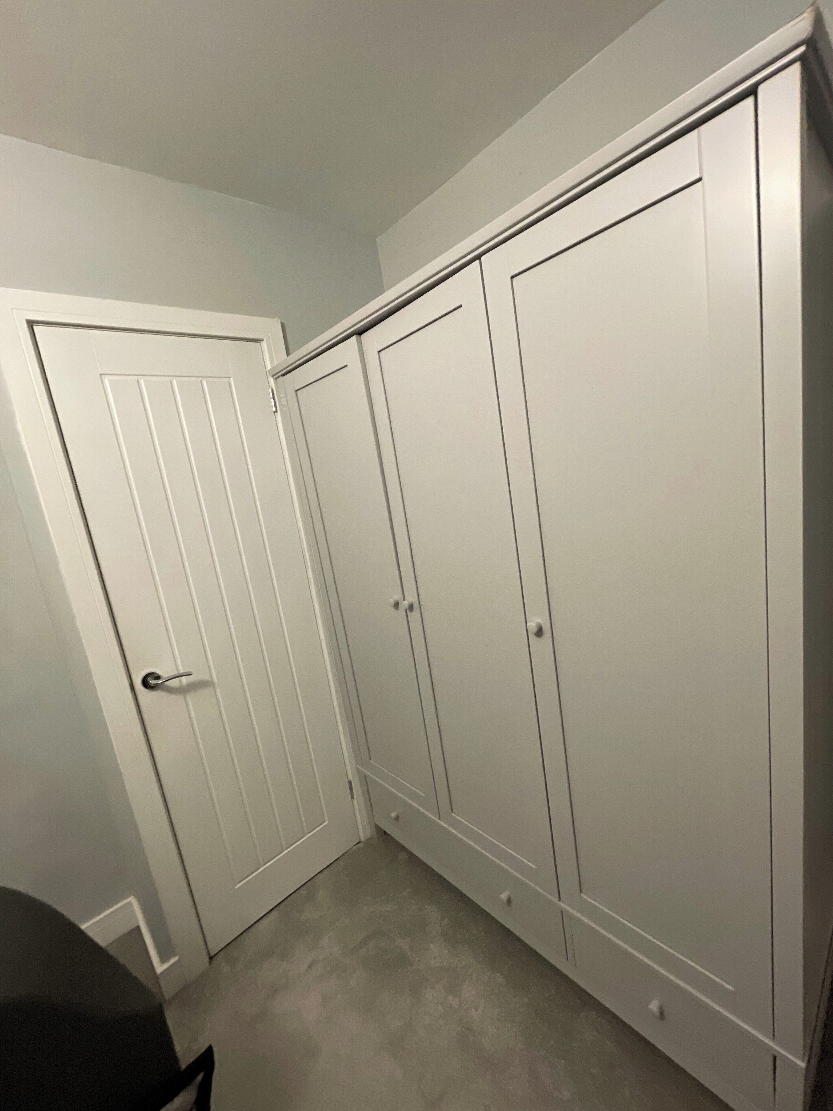 A room with a white door, a white wardrobe, and a grey carpet.