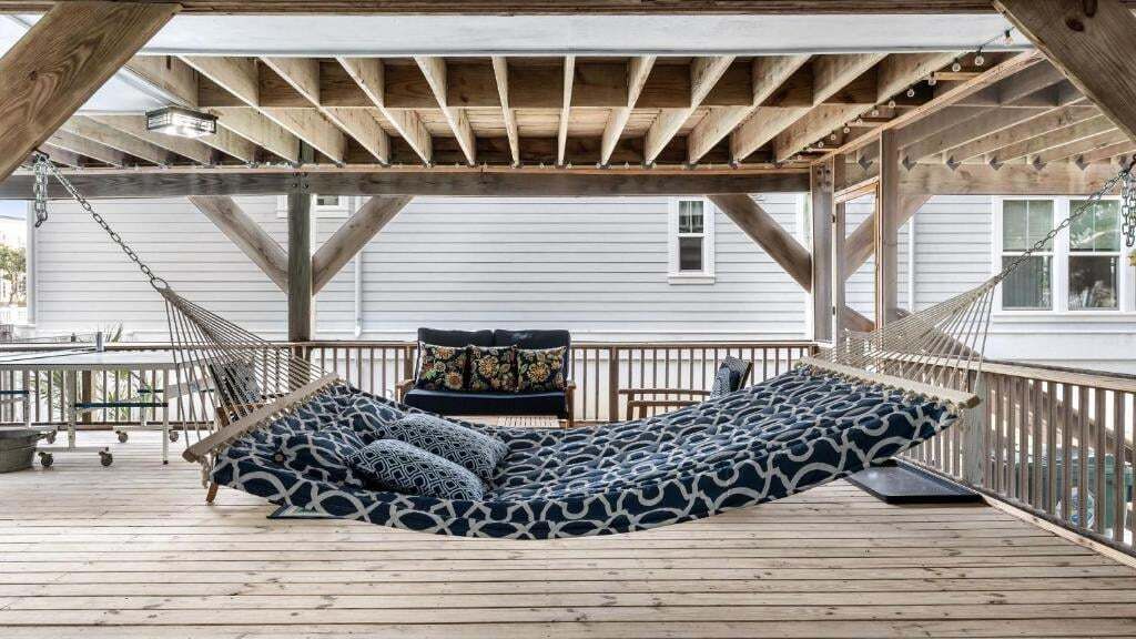 A hammock on a wooden deck with a railing, a bench, and a cushion.