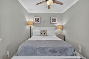 Ein Schlafzimmer mit einem Bett, zwei Nachttischlampen, einem Deckenventilator und gerahmten Bildern an der Wand.