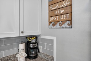 Eine Küche mit Kaffeemaschine, Küchenpapier und einem dekorativen Schild mit der Aufschrift 'Beach Life is the BEST LIFE'.