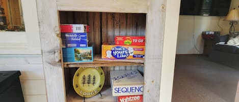 A wooden shelf with various board games and a plate with a forest design.