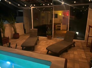 An outdoor patio with two lounge chairs, a pool, and a glass door leading to an interior space. - El Sol: apartment with rooftop lounge access minutes from 5 Avenida (Playa del Carmen)