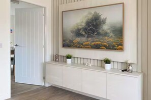 Een hal met een witte console tafel, een schilderij van een boom en landschap, en een deur naar een andere kamer.